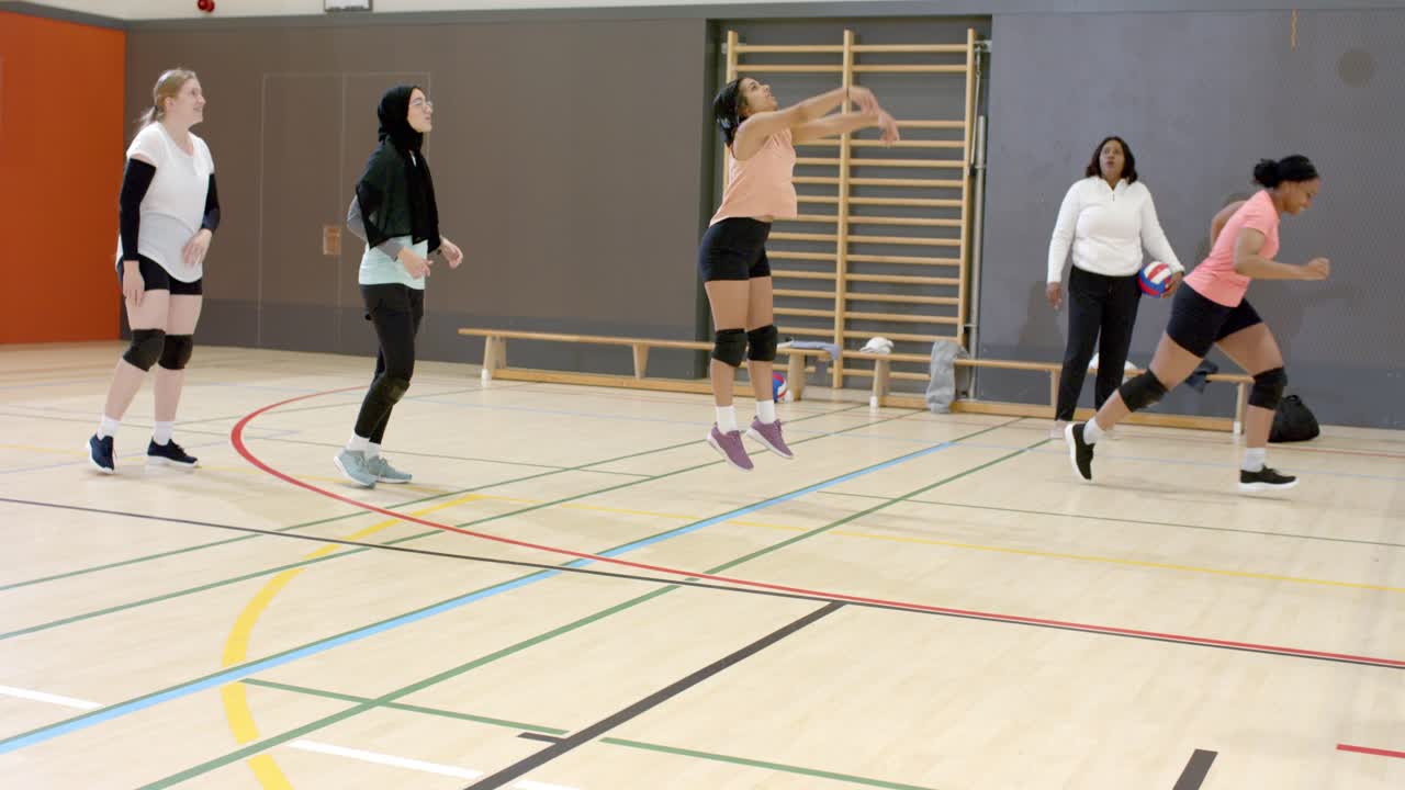 Diverse female teammates following female coach tossing volleyball passing, spiking rotation at gym