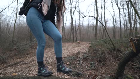 young caucasian woman photographer with hiking shoes walking and balancing on cut tree laying on leaf covered road in forest, slow motion