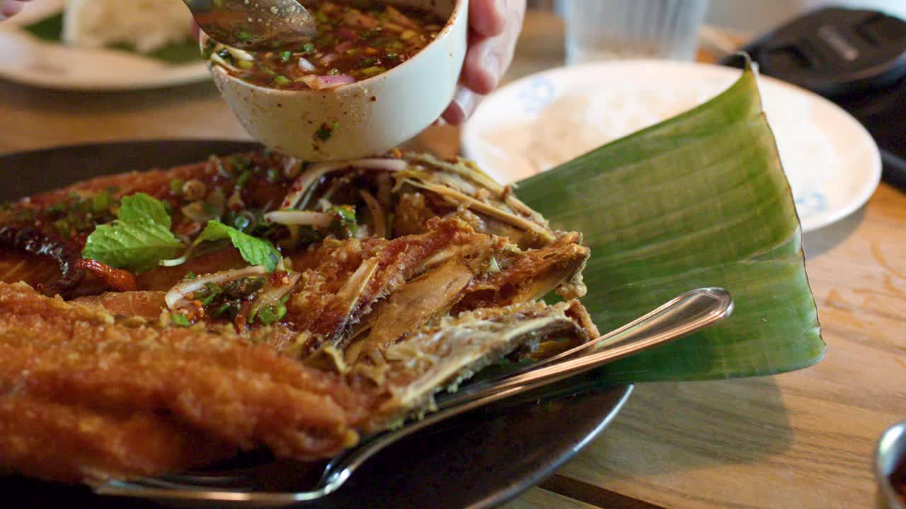 Spicy chili herb sauce poured onto crispy fried fish on banana leaf in natural light