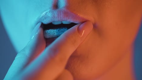 extreme close up of a beautiful woman lip while she takes a capsule in nightlife to stay fit for the evening in the club in slow motion