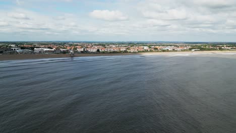 Typical-English-seaside-resort,-shot-using-a-drone-flying-into-the-sun-giving-a-aerial-viewpoint-with-a-wide-expanse-of-beach-with-a-pier-and-crashing-waves-3