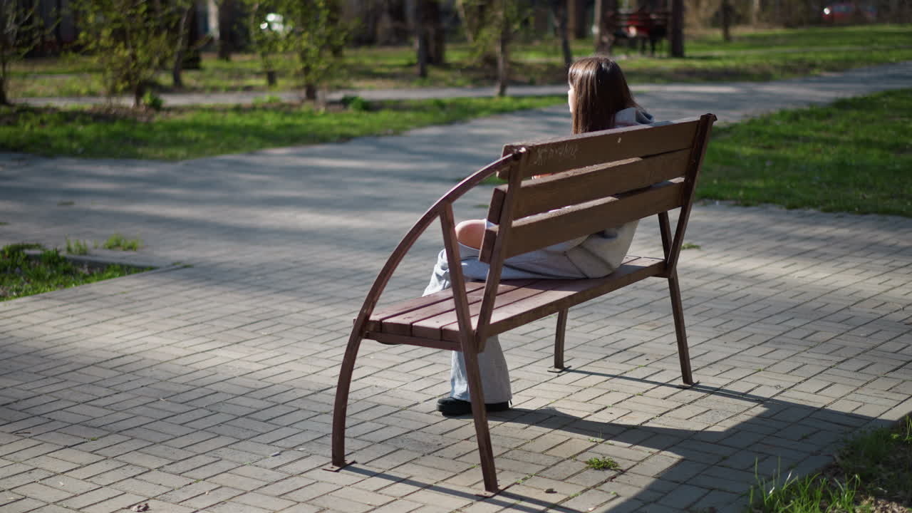 Joven descansando, chica sentada tranquilamente en un banco del parque, joven disfrutando de un entorno tranquilo y sereno en el parque, joven aprovechando un momento para relajarse en un parque al aire libre y apacible.