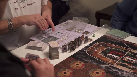 Hands-mixing-cards-of-board-game,-high-angle-closeup-view,-playing-area-and-people-around-table