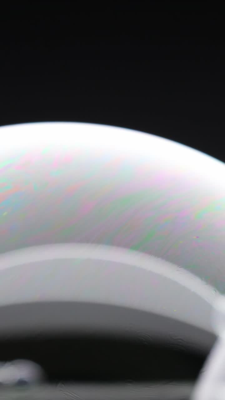Una bolla di sapone passa da trasparente a colori vivaci, evidenziando i riflessi di luce dinamici e la tensione superficiale.