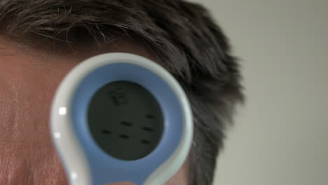 close up, middle aged man takes temperature with digital thermometer