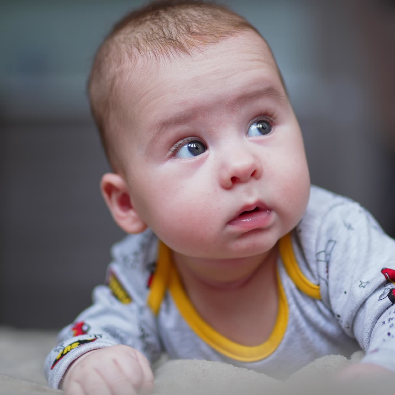 Little toddler boy lies on bed and looks up surprised. Cute close up portrait of a smiley baby. Blurred backdrop