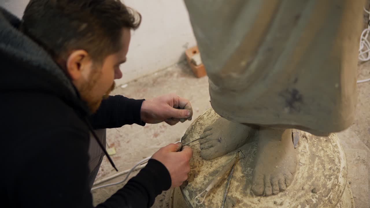High angle view of clay Buddha's statue feet, artist works with detail using tools