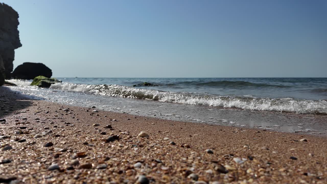 Nærbilde av bølger på en sandstrand med steiner