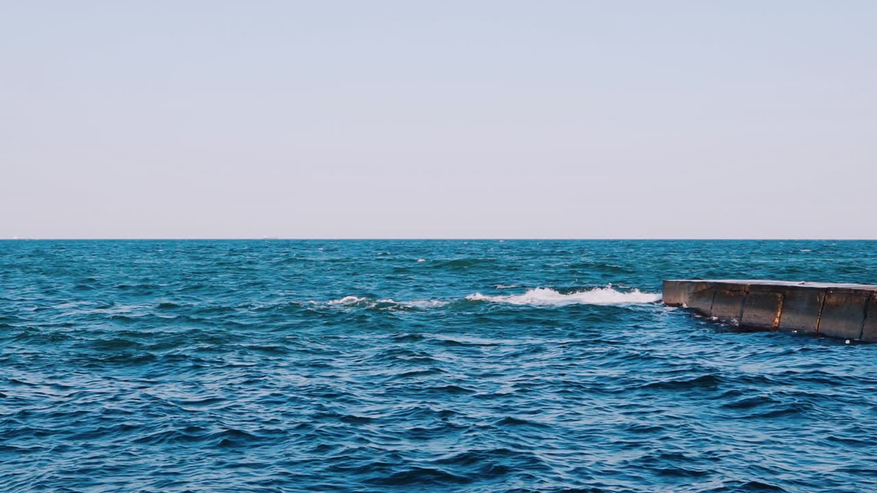 Blue seascape background. Motion of water waves in the sea. Stone dock in seawater. Slow motion.