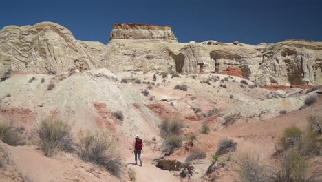 lonely female hiker with backpack walking on desert hiking trail under sandstone formations on hot sunny day