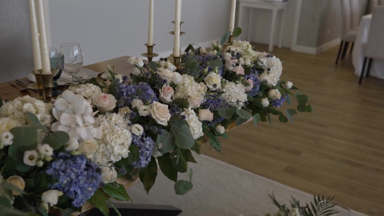 Elegante centrotavola floreale con rose bianche, ortensie blu e candele su un tavolo di legno in un allestimento per ricevimento di matrimonio.