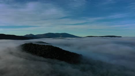 Vuelo-De-Drone-Sobre-Un-Mar-De-Nubes-En-Un-Valle-Al-Amanecer-Haciendo-Girar-Una-Cámara-Hacia-La-Izquierda-Con-Un-Cielo-Azul-Con-Nubes-Altas-Predominando-En-Las-Imágenes-Las-Diferentes-Tonalidades-De-Azul-En-Avila-España