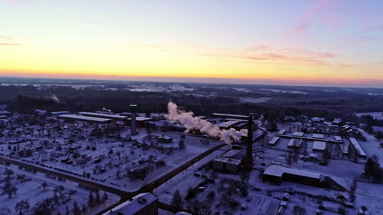 съемка с воздуха над городским пейзажем с заснеженными крышами и дымом из промышленной трубы на восходе солнца