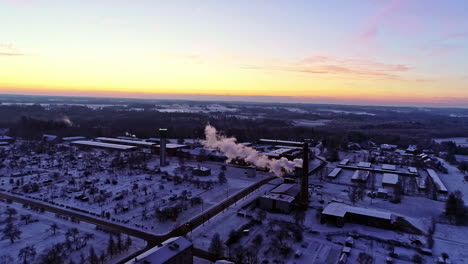 Luftweiterleitung-über-Stadtlandschaft-Mit-Schneebedeckten-Dächern-Und-Rauch-Aus-Einem-Industrieschornstein-Bei-Sonnenaufgang