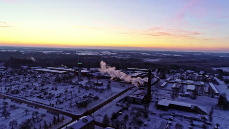 reenvío aéreo sobre el paisaje urbano con techos cubiertos de nieve y humo saliendo de una chimenea industrial al amanecer