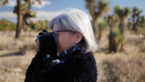 An-adult-woman-photographer-taking-pictures-with-her-old-fashioned-film-camera-and-lens-in-a-desert-wildlife-landscape-CLOSE-UP