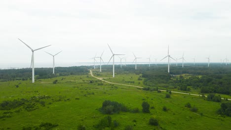 aerial drone footage slowly and smoothly flying in front of a large green and misty fog covered peninsula that has dozens od electric energy generating renewable wind turbines spinning on it. roads