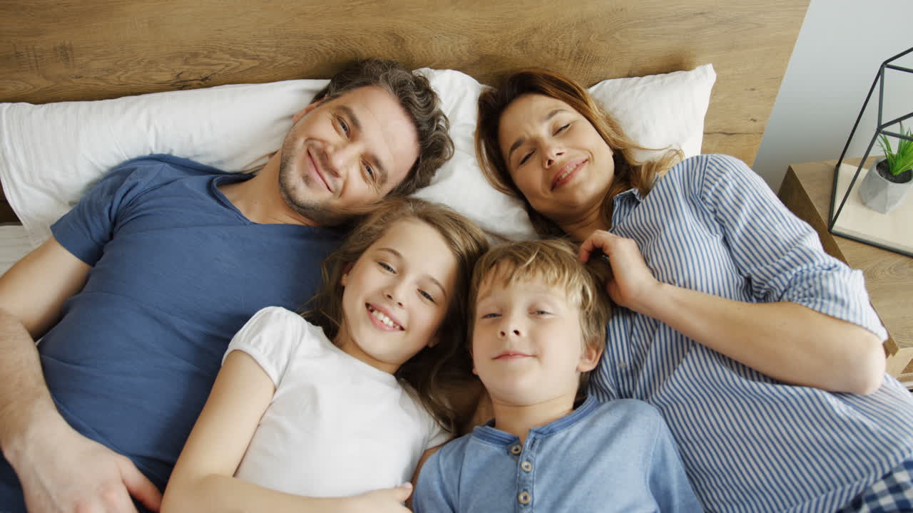 vista superior de padres felices con sus hijos acostados en la cama, abrazándose y sonriendo a la cámara por la mañana