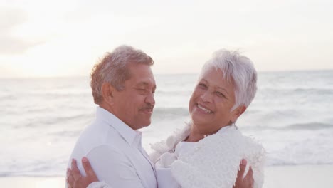 Porträt-Eines-Glücklichen-Hispanischen-Frisch-Verheirateten-älteren-Paares,-Das-Sich-Bei-Sonnenuntergang-Am-Strand-Umarmt