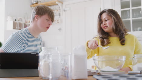 Una-Pareja-Joven-Con-Síndrome-De-Down-Sigue-Una-Receta-En-Una-Tableta-Digital-Para-Hornear-Pasteles-En-La-Cocina-De-Casa