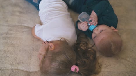 Entzückendes-Baby-Trinkt-Wasser-Und-ältere-Schwester-Liegt-Auf-Dem-Bett