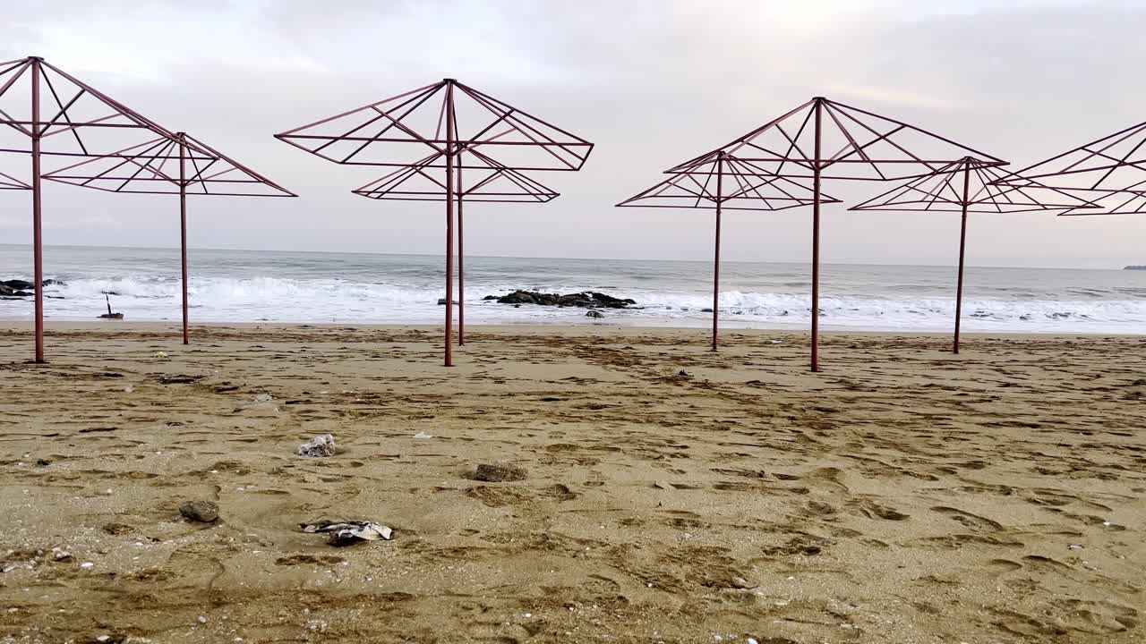 Nogle metalparasoller står på stranden, mens bølgerne slår mod sandet tidligt om morgenen