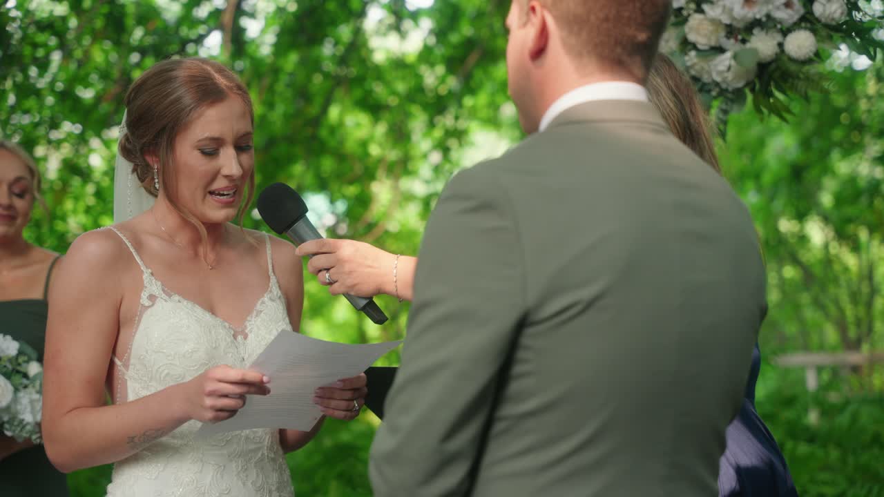 Bride reads vows to groom, looks up and smiles, while maid of honor wipes tears