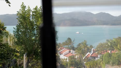 Pan-out-of-golf-buggy-cart-to-reveal-white-stucco-houses-and-tropical-island-view-with-boat-in-water-on-Hamilton-Island,-Australia,-Queensland