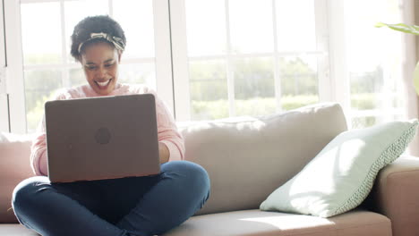 mujer afroamericana se ríe mientras usa una computadora portátil en un sofá en casa con espacio para copiar