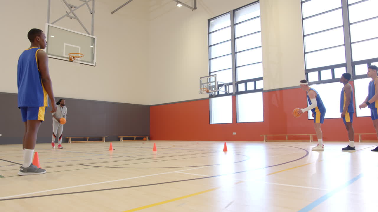 Dribbling around cones, players practicing basketball drills in gymnasium