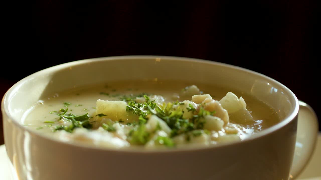 Nærbillede af varm cremet chowder med brødtern og krydderurter, varmt naturligt lys, minimal bevægelse