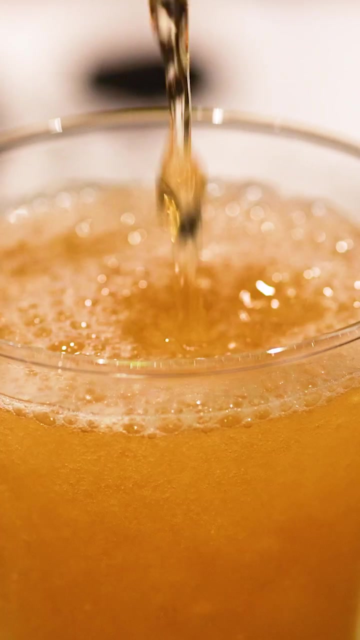 Birra dorata versata in un bicchiere, che forma una schiuma densa sotto un'illuminazione calda. Una vista ravvicinata cattura le bollicine effervescenti.