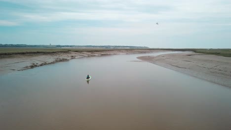 Man-kayaking-on-meandering-river,-drone-pans-to-the-left-with-beautiful-landscape-in-the-background