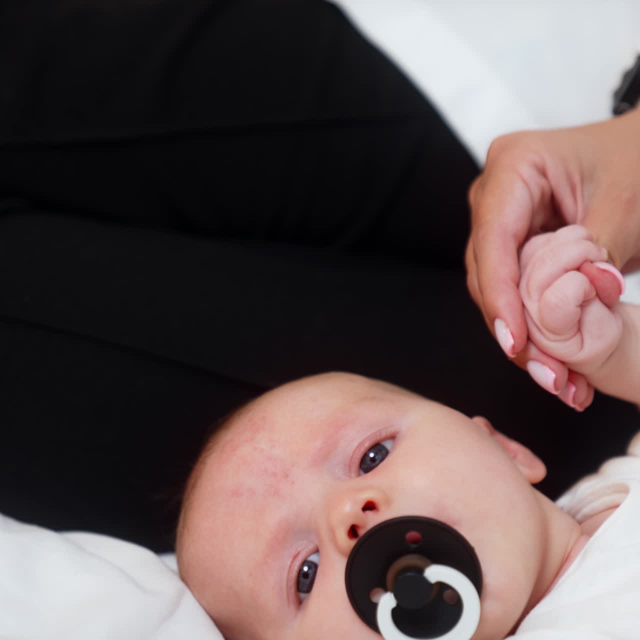 Lovely newborn with a pacifier in mouth. Mom holds a tiny baby hand. Close up