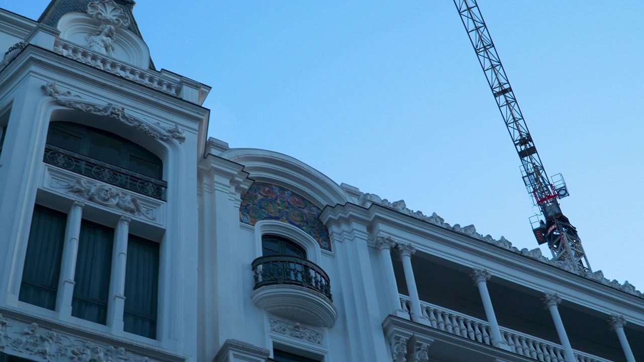 Toma en ángulo bajo de la fachada de un edificio clásico europeo en Madrid, con intrincados tallados y balcones, junto a una moderna grúa de construcción durante la hora azul.