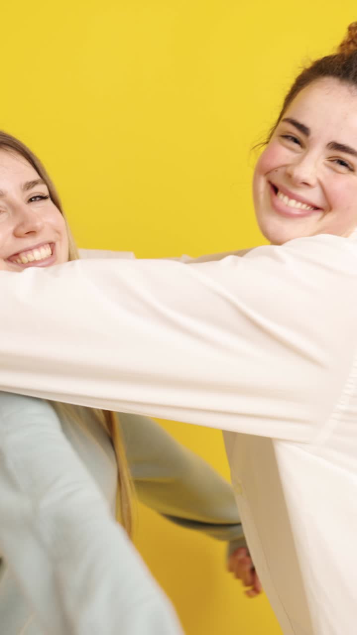 Young women embracing each other on yellow background