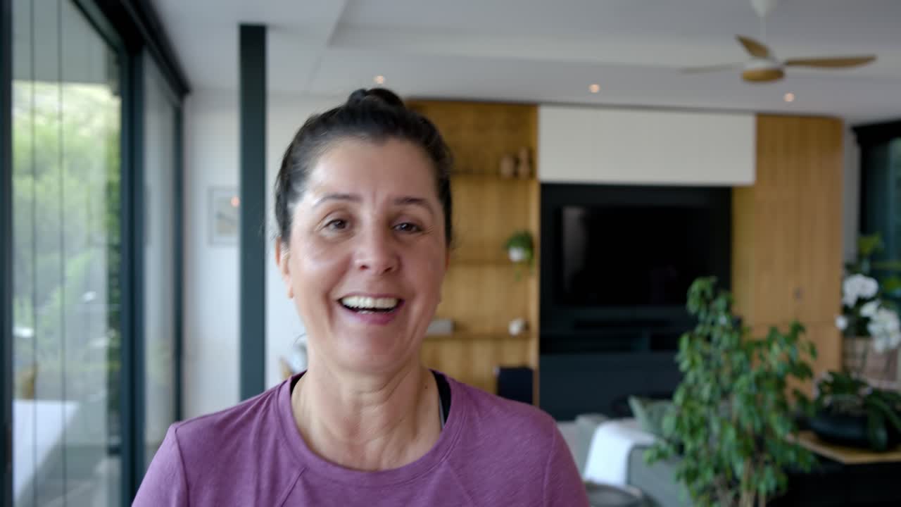 Donna con un top viola che guarda il verde del balcone, si volta verso la telecamera, sorride e ride a casa