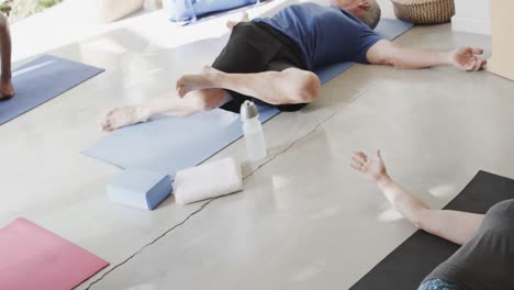 diverse seniors practicing pilates lying on mats with female coach, unaltered, in slow motion