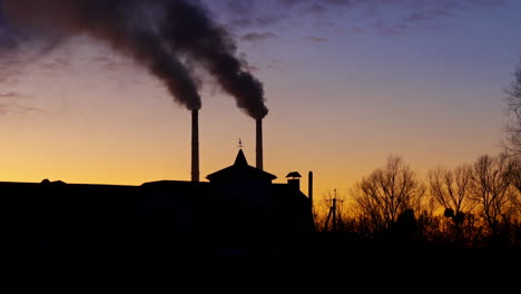 silhouette of the building in the evening. two plant pipes are producing the heavy smoke.