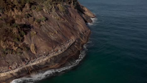 Rückwärtsbewegung-Aus-Der-Luft,-Die-Wellen-Entlang-Des-Leme-Felsens-Am-Ende-Des-Copacabana-Boulevards-Folgt-Und-Menschen-Am-Rand-Des-Hügels-Und-Am-Strand-Im-Vordergrund-Enthüllt