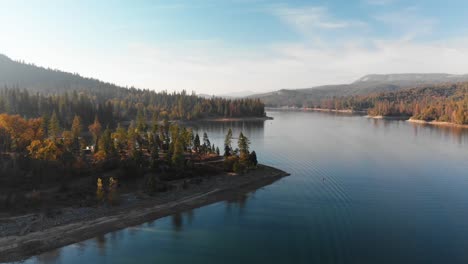 Aerial-shot-of-a-beautiful-blue-alpine-lake-surrounded-by-pine-trees,-mountains,-and-cloudy-sky