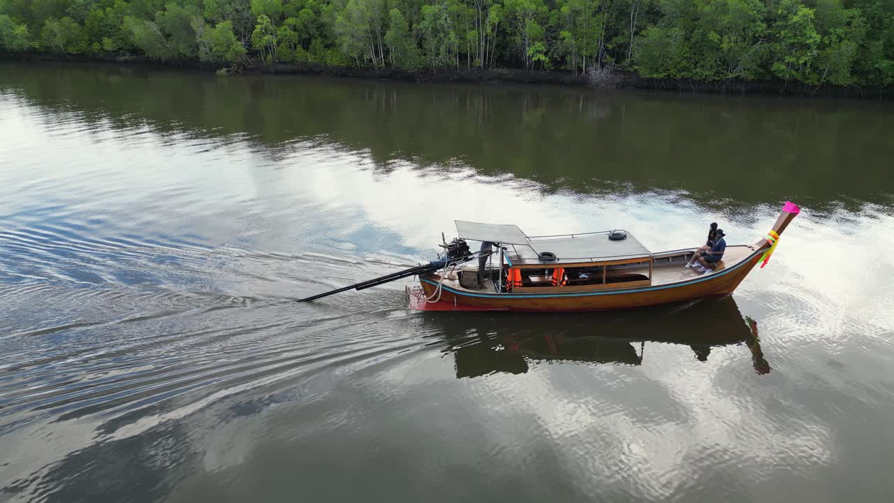 Low aerial orbits long-tail boat in mangrove river channel, Thailand