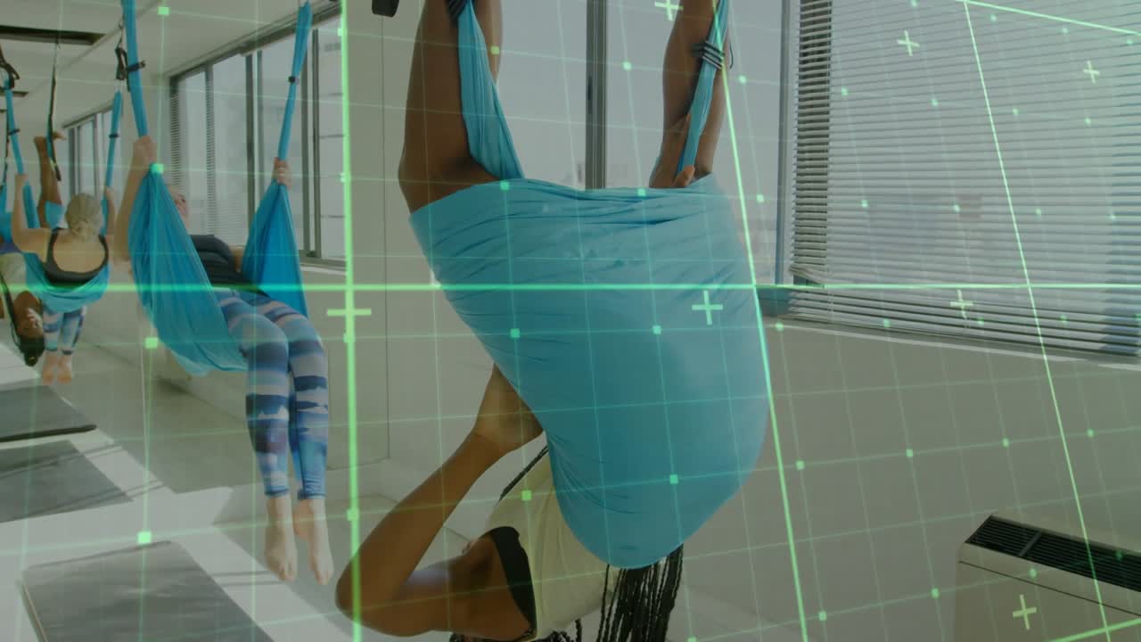 Mulher em primeiro plano segurando as alças e girando para uma inversão em yoga aéreo, enquanto uma grade de RA guia o alinhamento.