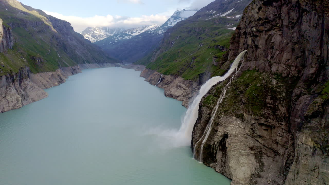 Stunning FPV and drone shots soaring through the Swiss Alps, capturing the Mauvoisin Dam and its majestic waterfall on a clear, sunny summer day.