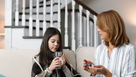 白人女人坐在她病的女儿旁边喝水