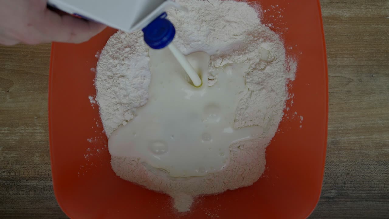 verter leche en un cuenco de harina mientras se prepara la masa para los productos horneados caseros