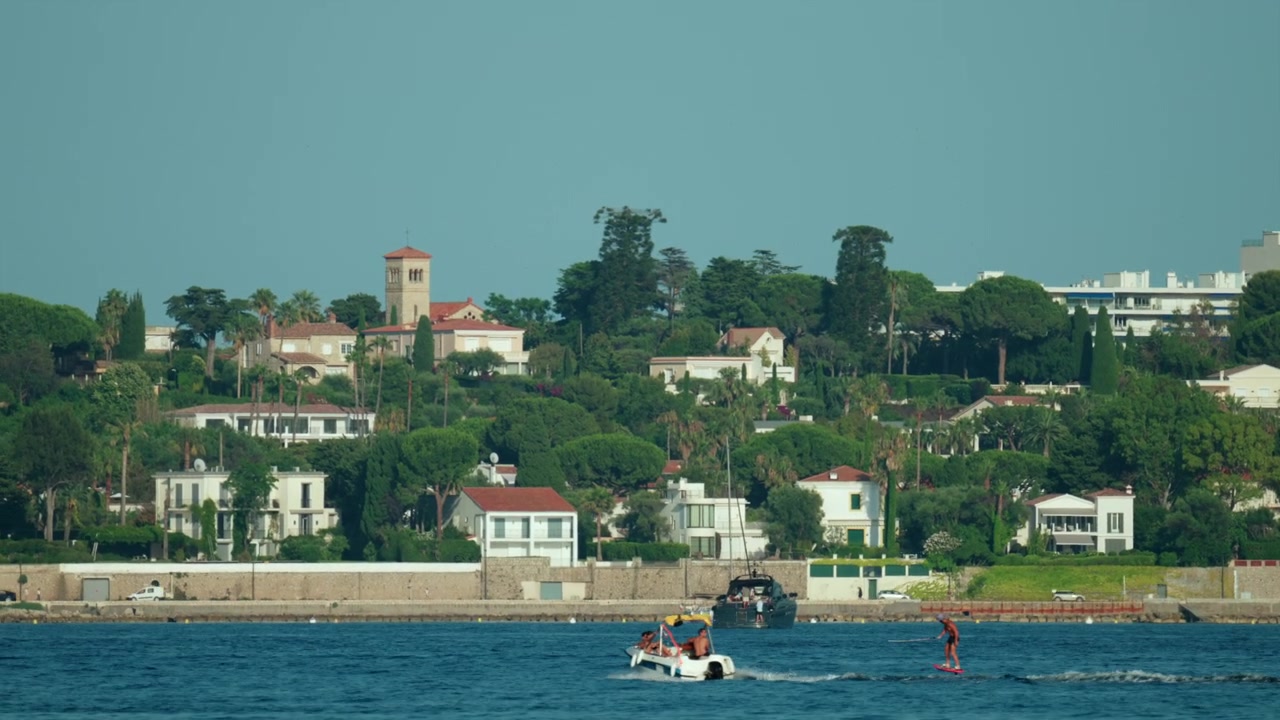 Costa della Costa Azzurra con ville lussuose e vegetazione lussureggiante lungo il Mar Mediterraneo, persone che si godono un giro in barca e sport acquatici, Antibes, Francia