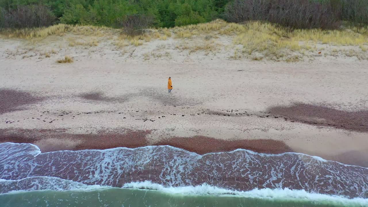 Woman is walking on the wild beach. Bright coat. Gloomy day.