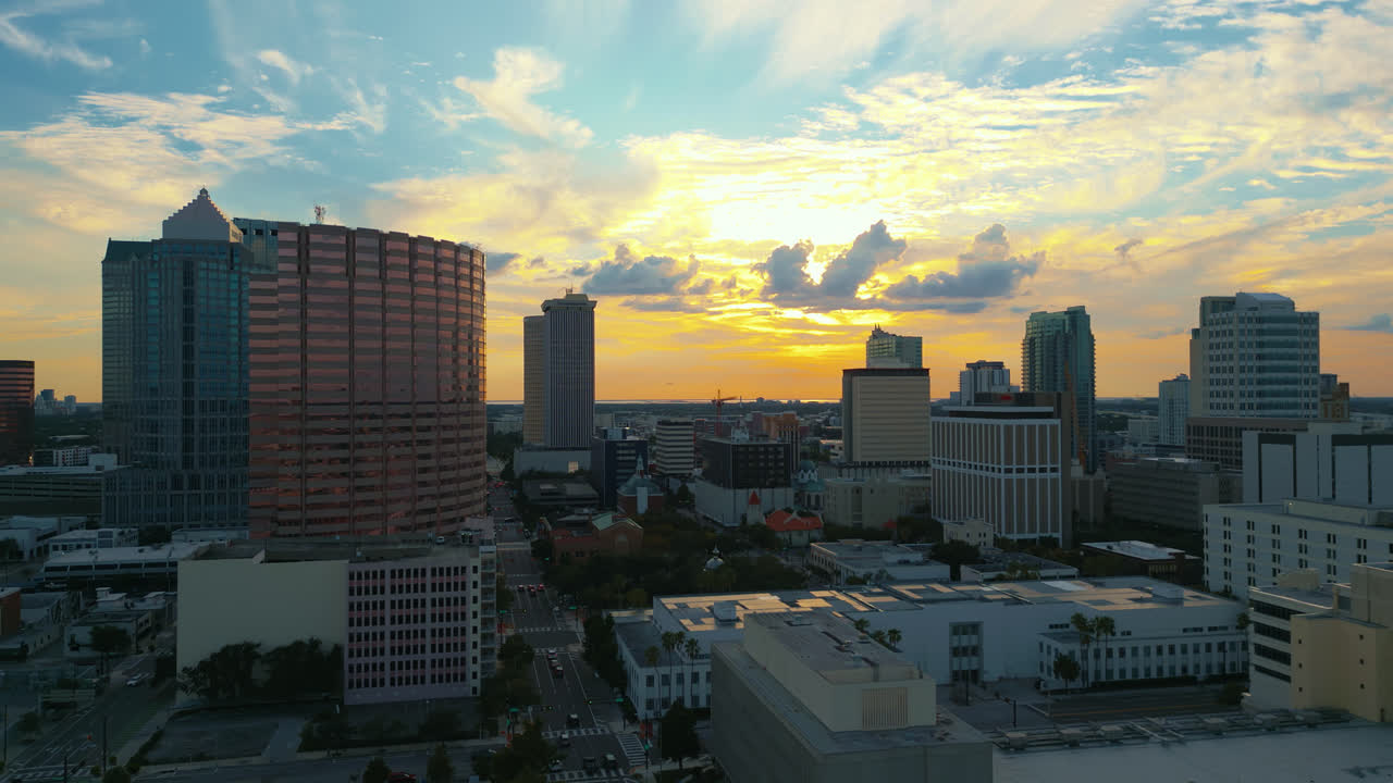 Golden sunset light illuminating the Tampa skyline buildings with beautiful colors in the sky and cars drive down the road. Aerial tracking right shot