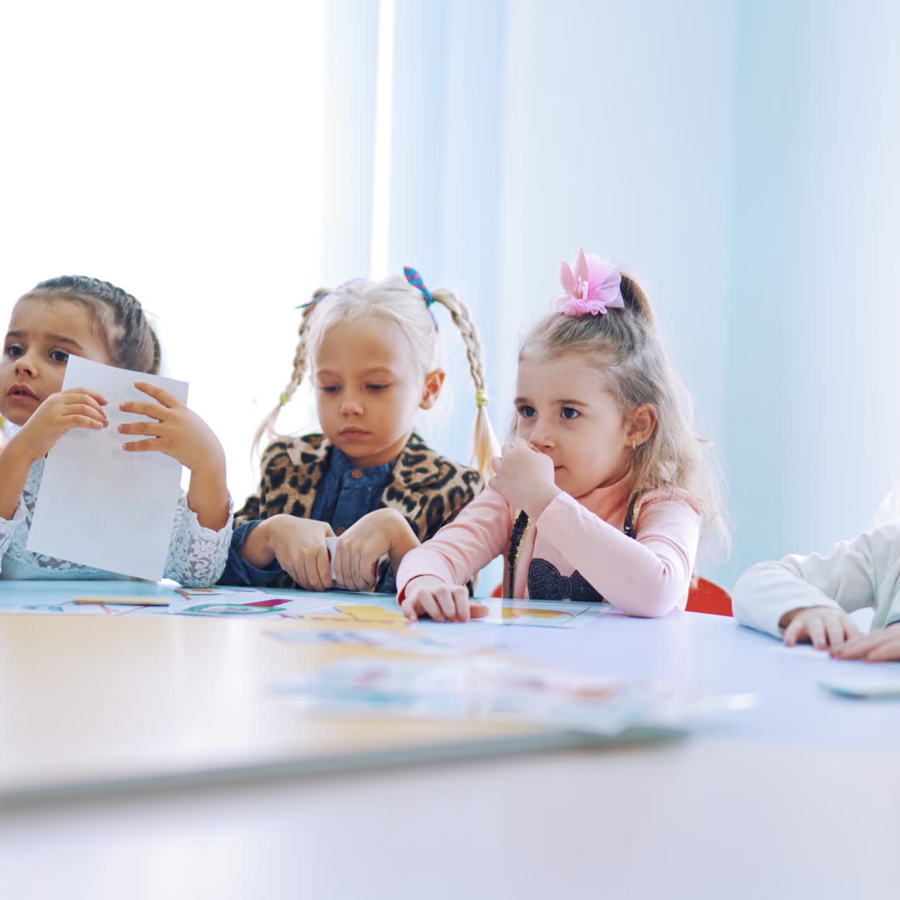 Little children studying at the lesson. Elementary school children sitting together at the round table and working with paper pictures. Small girl gives one card to her teacher.